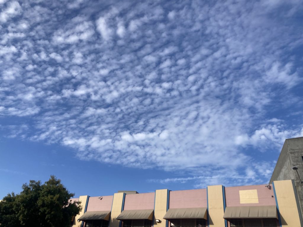 Bright blue sky with cottony clouds above a pink and yellow building with brown awnings