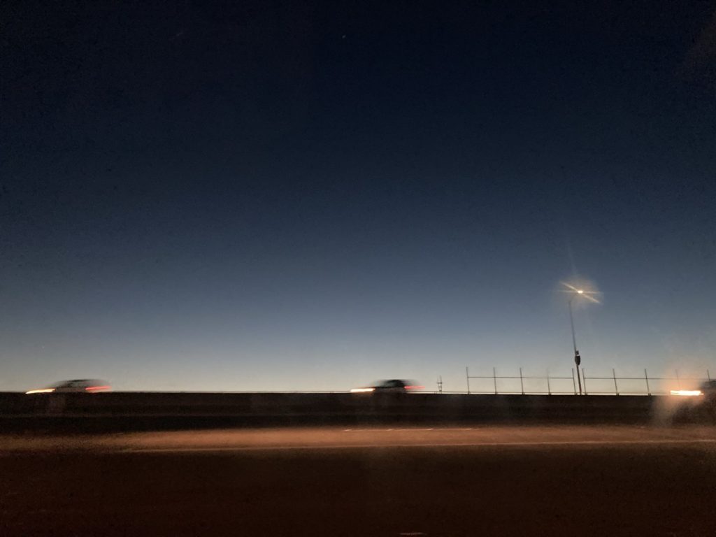 Highway at dusk, cars with headlights on streak across the road