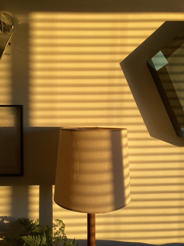 Lines of golden yellow light on the wall, a lampshade casts a shadow. 
