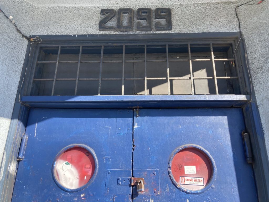 Top portion of blue double doors with porthole windows; they’re padlocked together. Above the doors, the number 2099.