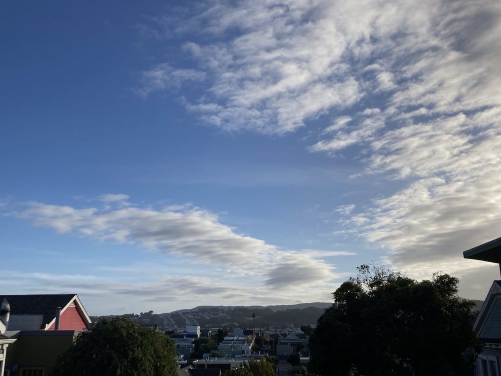 Blue sky with wispy white clouds across the right half the frame. The red peak of a house is visible on the left