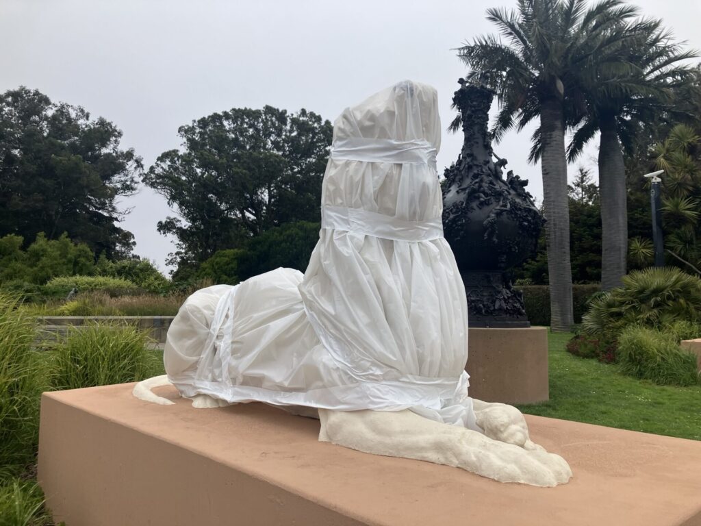 Outdoors, a white statue of a resting animal covered in white plastic.
