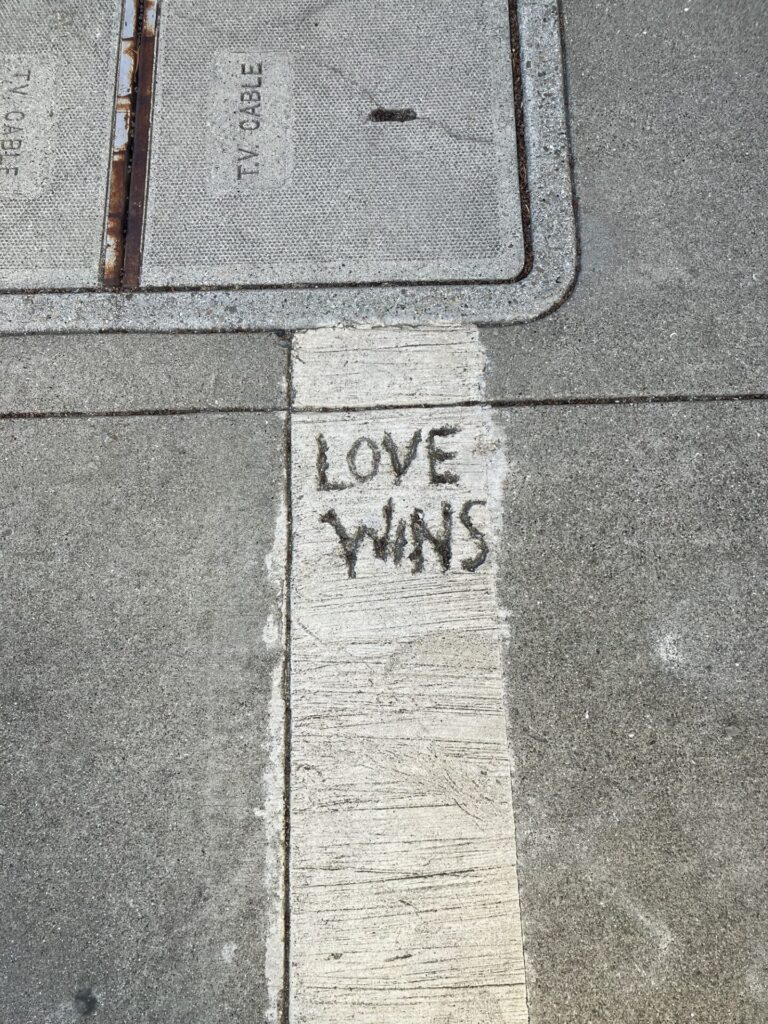 Sidewalk with long narrow patch of slightly light gray, in which someone has written LOVE WINS.