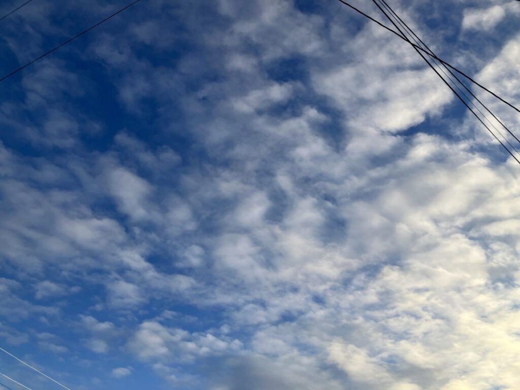 Light clouds on blue sky. In the upper right corner are some power lines. 