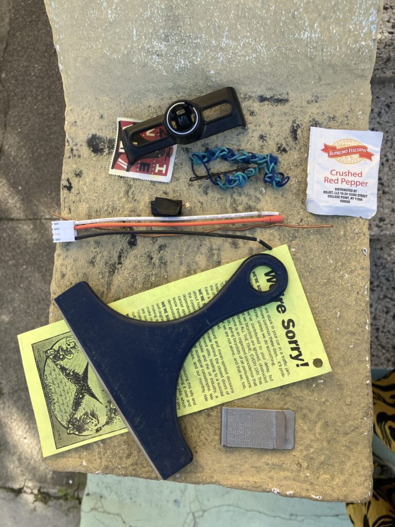 Pile of random stuff including crushed red pepper packet, squeegee, colored wires, and yellow pamphlet with the title “We’re sorry”.