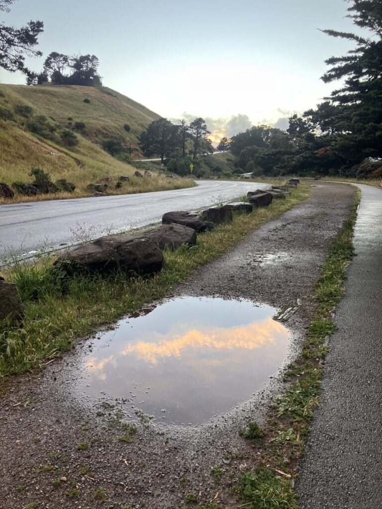 Large puddle between road and sidewalk reflecting the shimmery clouds.
